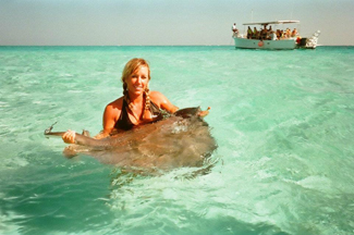 A photograph shows a woman standing in the ocean holding a stingray.