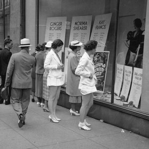Large downtown department stores emerged in the Interwar years as temples to consumerism. Window shoppers outside Simpson's in Toronto are offered styles alongside the sizing details of Hollywood's first generation of stars (including Canadian Norma Shearer).