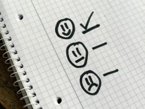 Three faces drawn on paper. One is happy, one is indifferent and one is uphappy. A checkmark is next to the happy face.