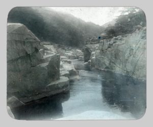 A colorized photograph of Kisō River by John Cooper Robinson. Striking rock formations buffer the river.