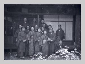 In the photo, a group of fifteen Japanese men and women pose outside a house.