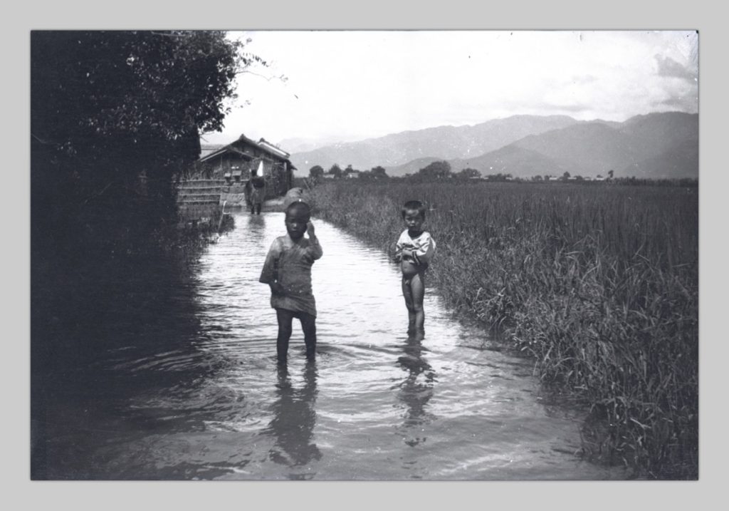 In this photo taken by John Cooper Robinson, two Japanese children stand in the ankle-deep water of an irrigation canal.