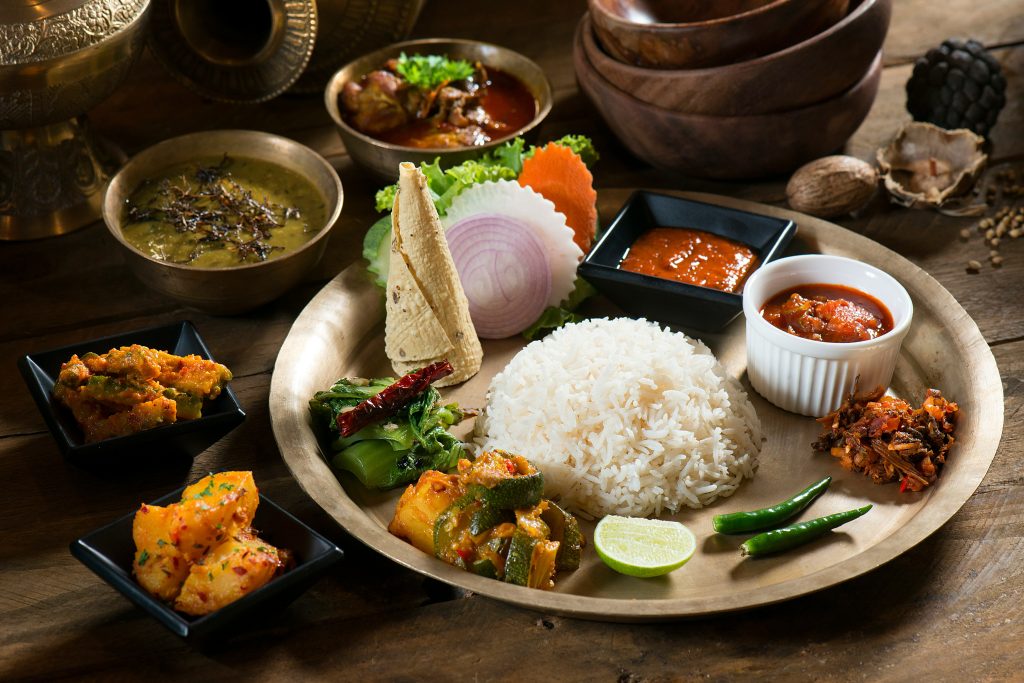 Nepali thali on a brass plate with rice, vegetable curry, pickles, greens, papad, onion, lime, and chilies.