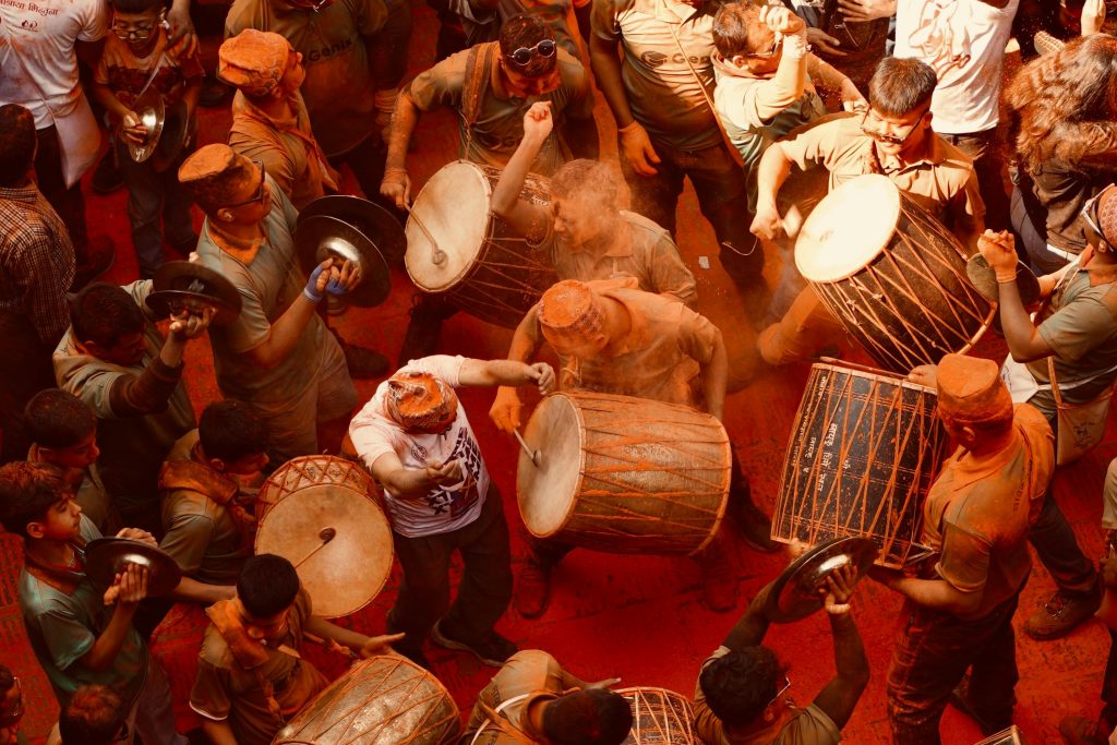 Musicians and a crowd celebrate Sindoor Jatra (festival) in Madhyapur Thimi, Nepal, with large drums and people covered in red vermilion powder.