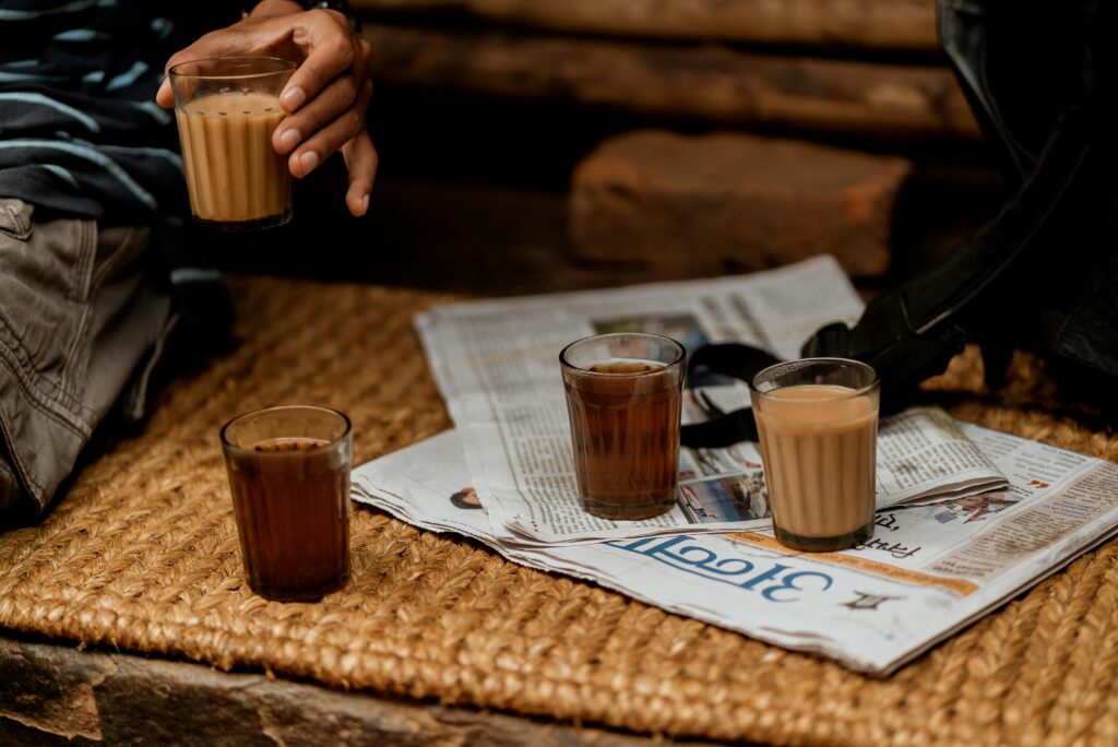 Glasses of Nepali milk tea on a woven mat, with a newspaper nearby.