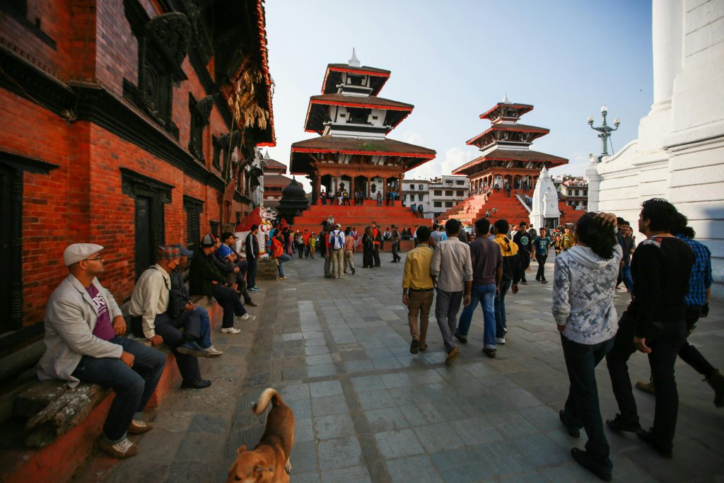 Historic street view of Durbar Square in Kathmandu, Nepal, with traditional temples and pedestrians in daylight.