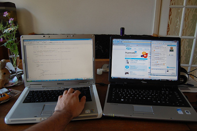 Two computers side by side, one with work on the screen, and the other with social networking