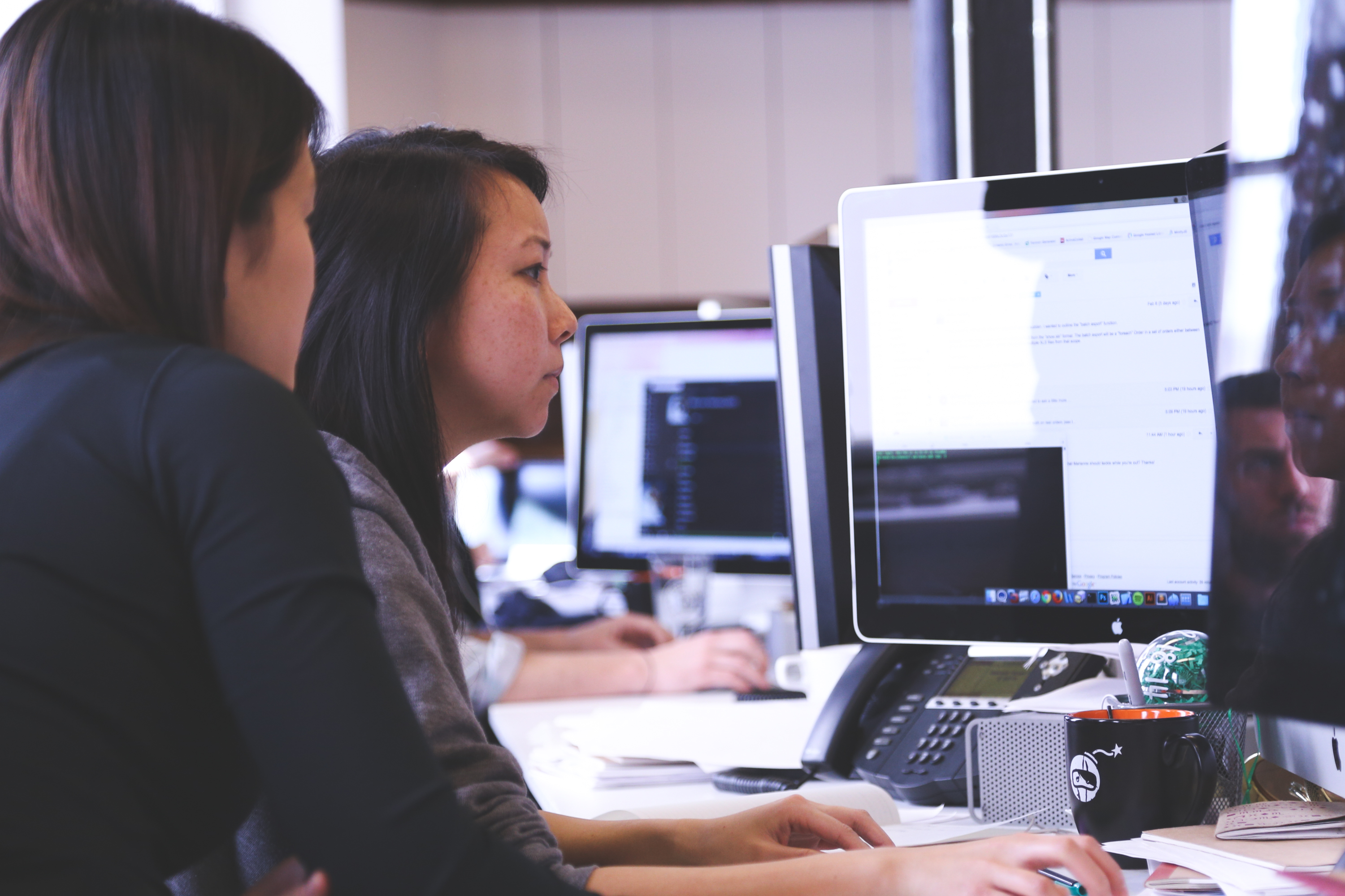 A woman helping a fellow coworker whil she works on a computer