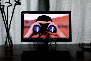 Person holding binoculars with the facebook logo in each eye: Facebook is watching you