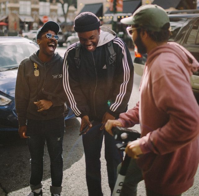 3 men in jackets standing on a street in a city and laughing