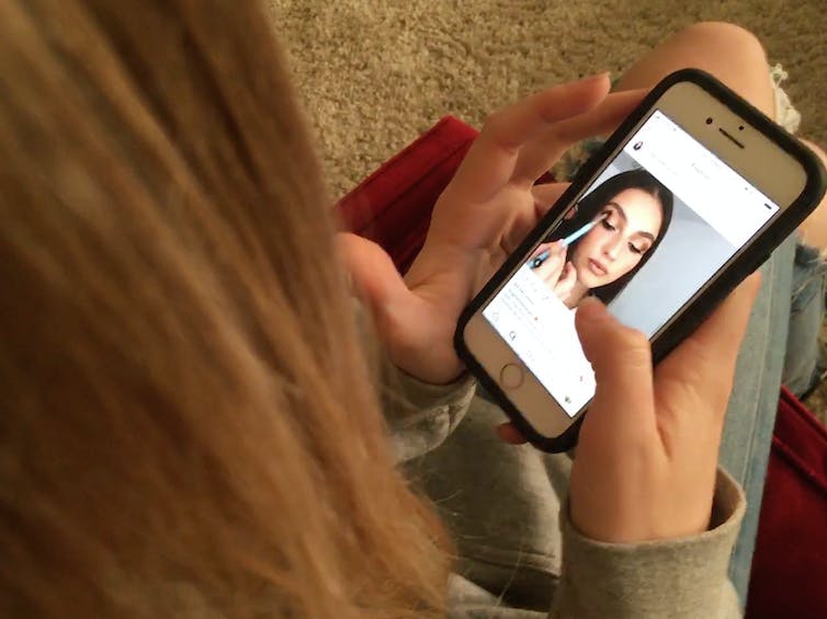 A teen watches an Instagram post of a young woman applying makeup