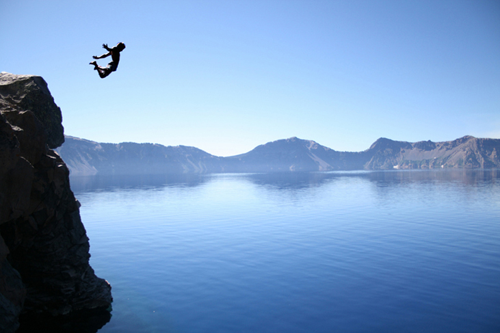 A photograph of a person jumping off a high cliff into a lake.