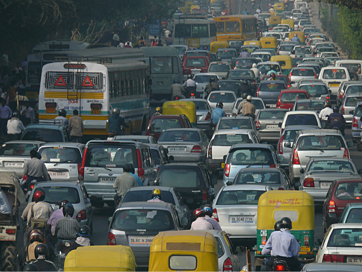 Photograph shows a roadway crowded with cars and motorcycles in Delhi.
