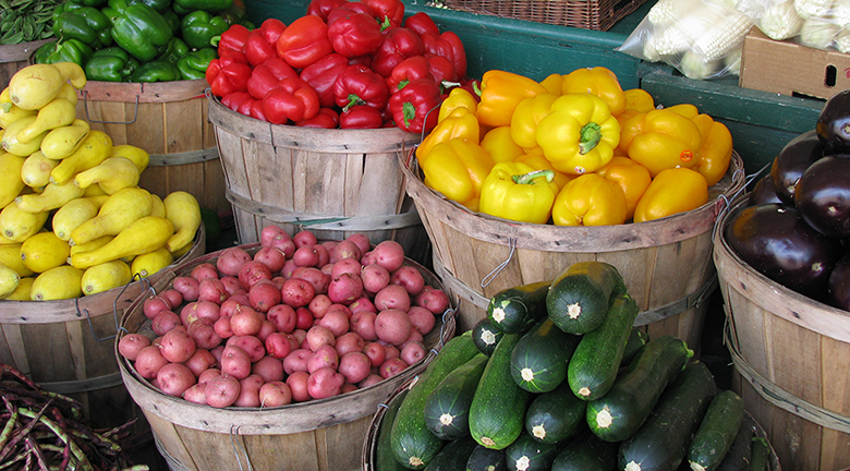This is a photograph of various organic vegetables in baskets at a farmer's market.