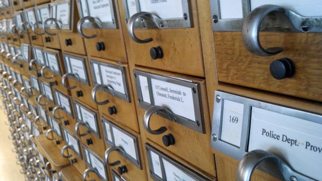 A close-up image of a library card catalogue shows dozens of drawers. The angle of the shot alludes to the hundreds of references for library materials each drawer contains.