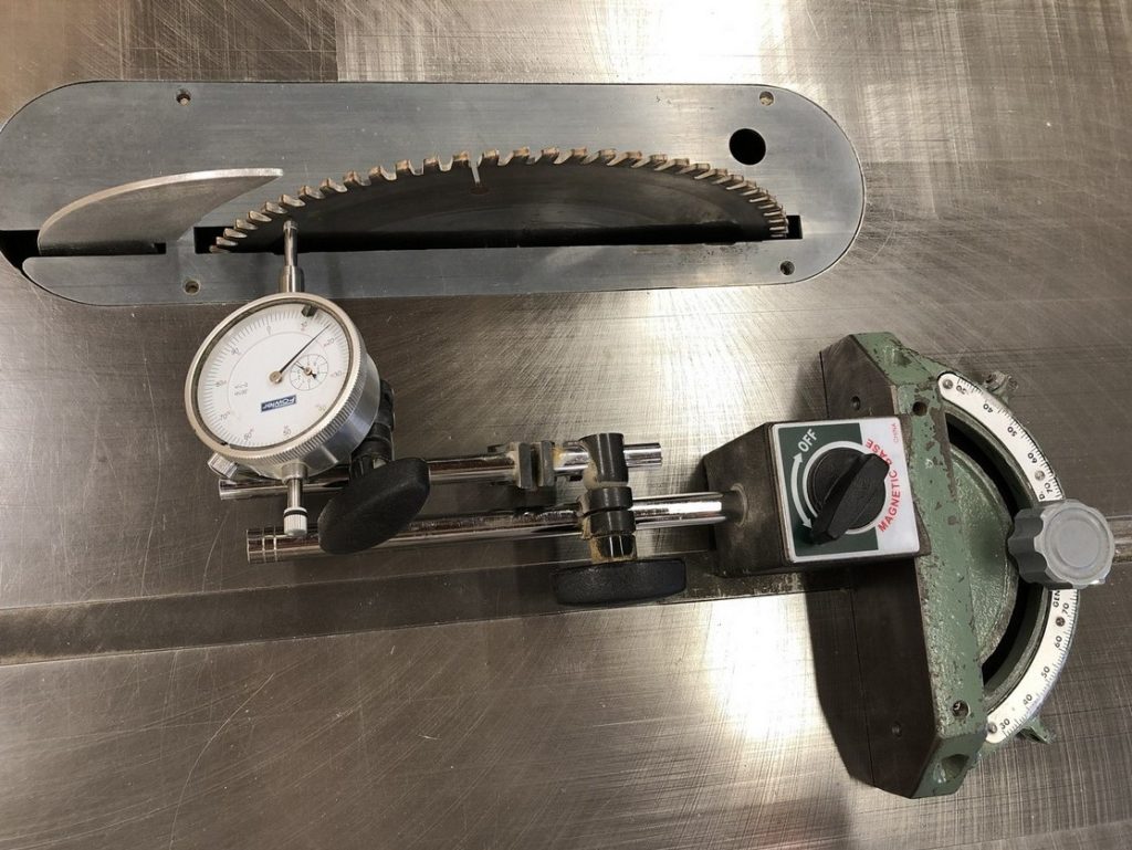Dial indicator attached to mitre gauge, with dial touching the saw blade at the back of the blade
