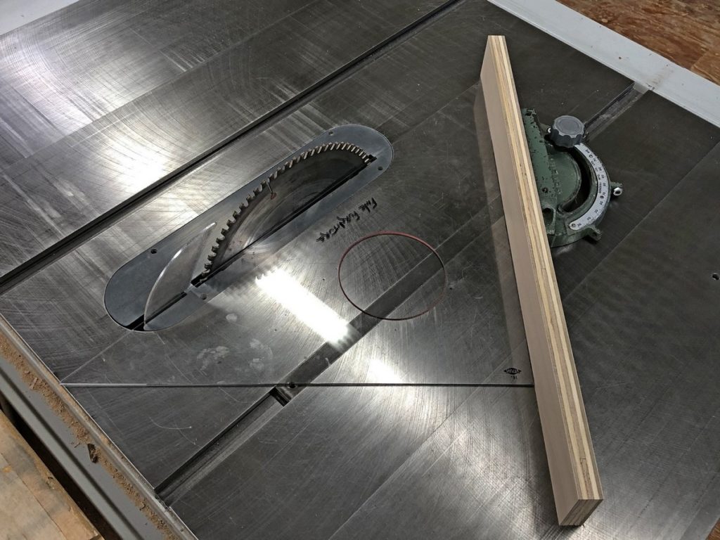 A drafting set square is placed touching the saw blade and mitre gauge at 45 degrees