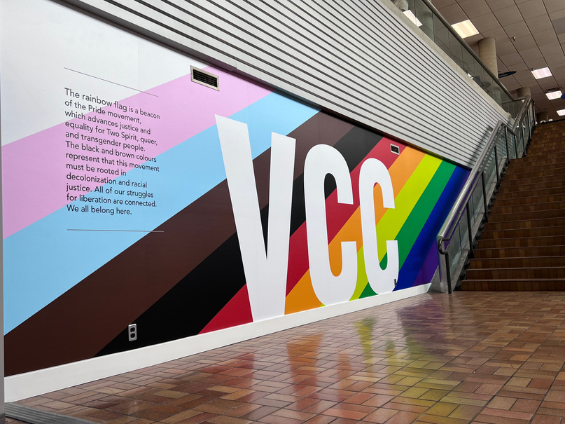 Rainbow mural at VCC Downtown campus. Reads: The rainbow flag is a beacon of the Pride movement, which advances justice and equality for Two Spirit, queer, and transgender people. The black and brown colours represent that this movement must be rooted in decolonization and racial justice. All of our struggles for liberation are connected. We all belong here.